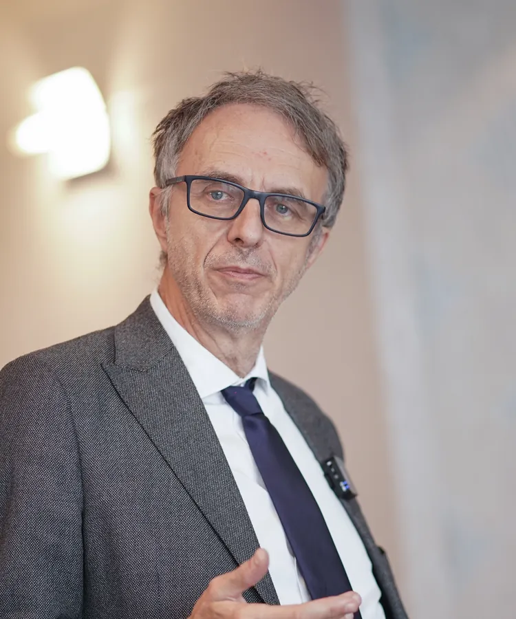 Portrait of Dr. Marco Paret, wearing glasses and a grey jacket, speaking