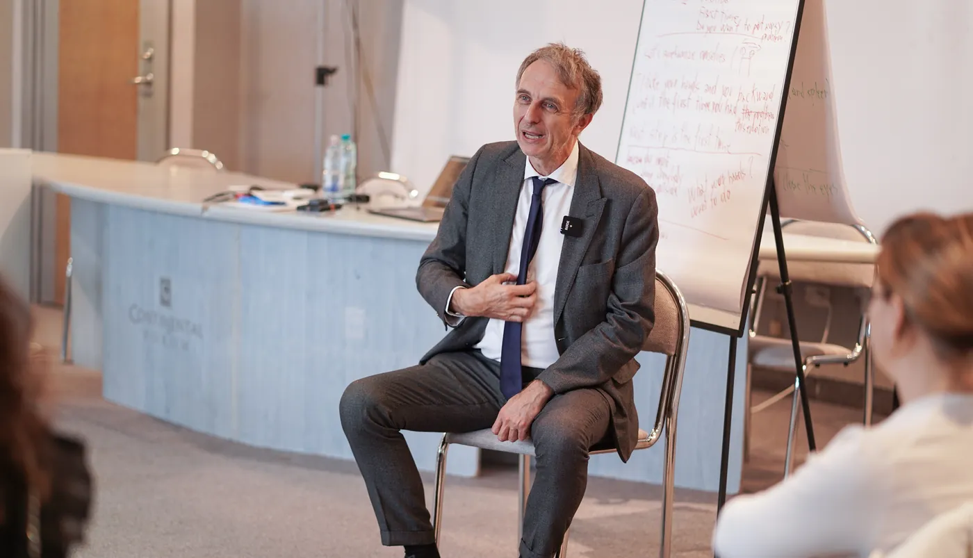 Dr. Marco Paret seated beside a flip chart, explaining a technique to participants seen from behind